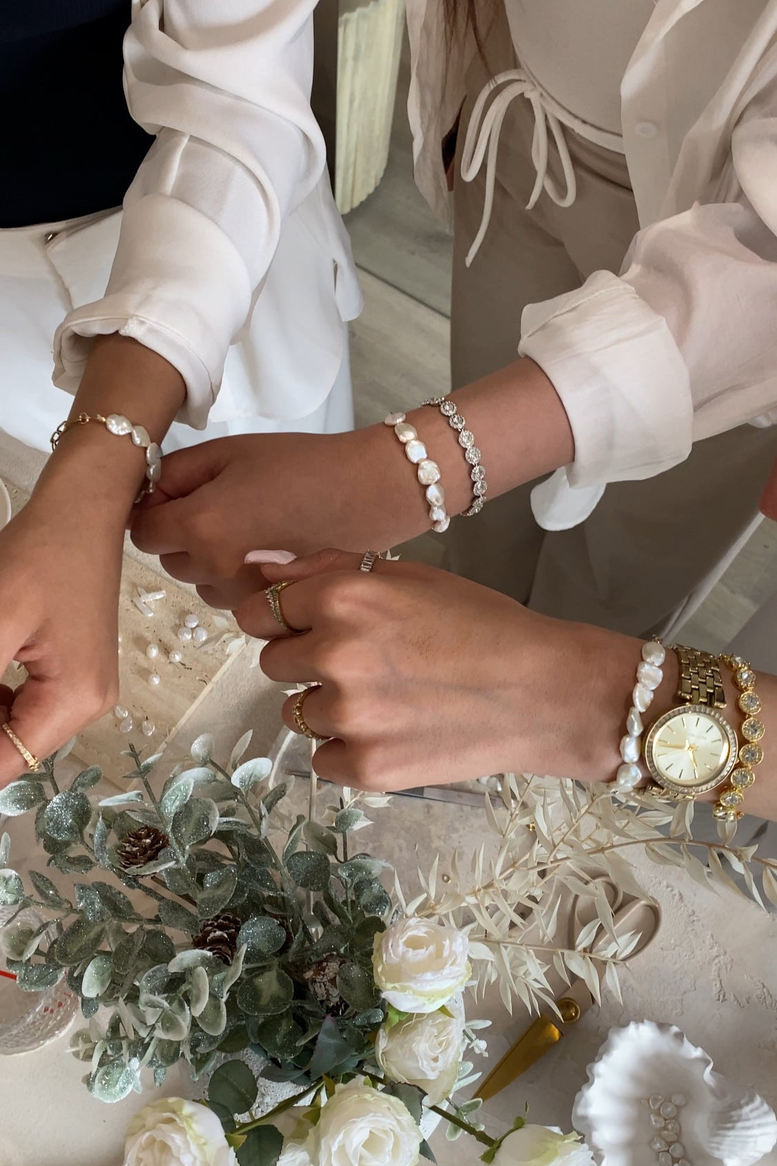 Two people holding hands with wedding rings, surrounded by flowers and jewelry.