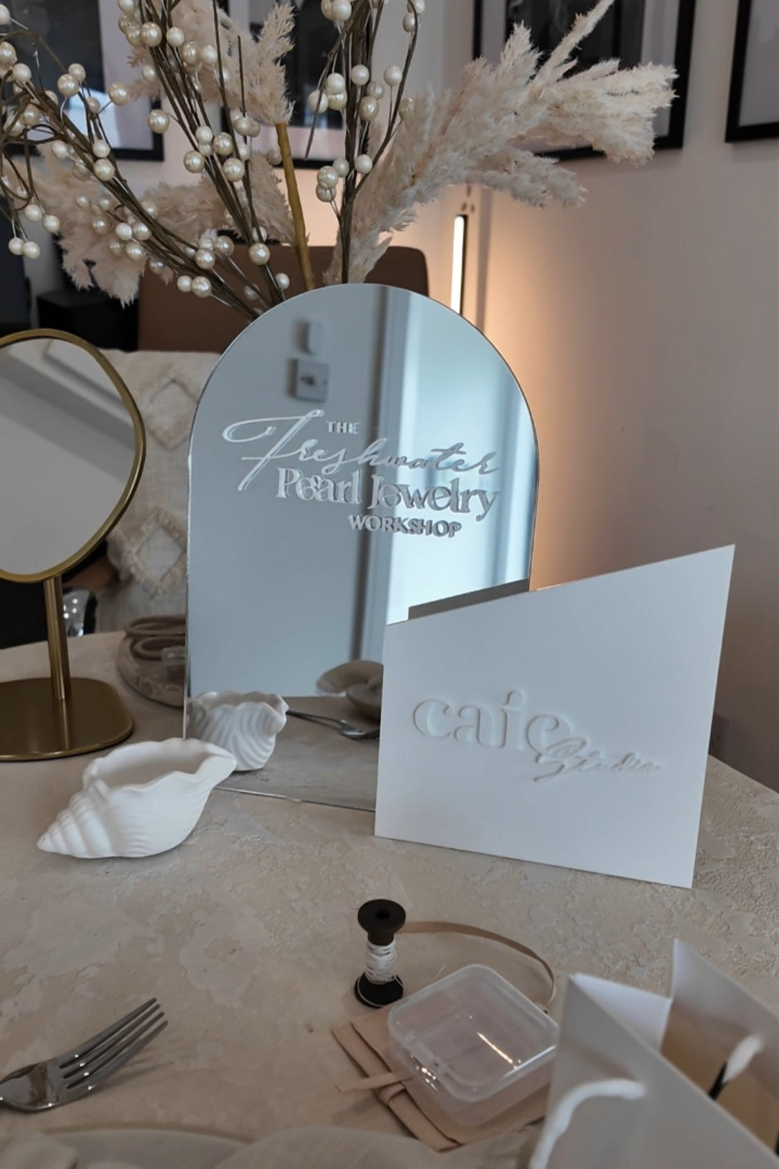 Table setting with a mirror, card, and decorative items on a tablecloth.